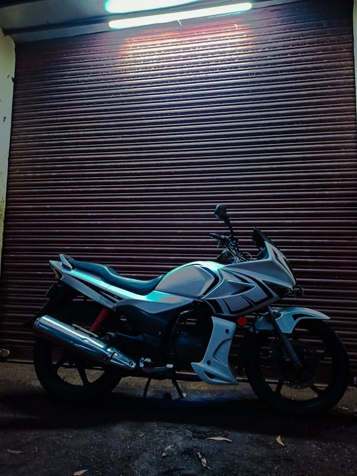 A modern white motorcycle parked against a closed garage door at night, illuminated by light.